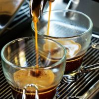 Fresh espresso being pulled into two short glass cups with handles