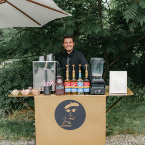 Espresso Dave Coffee Catering Barista dressed in black uniform standing behind gold mobile espresso bar with black logo.