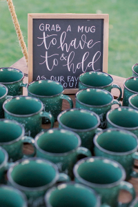 Green custom reusable coffee mugs on table with sign saying Grab a Mug is great customizable, personalized sustainable catering option for Espresso Dave's Coffee Catering.