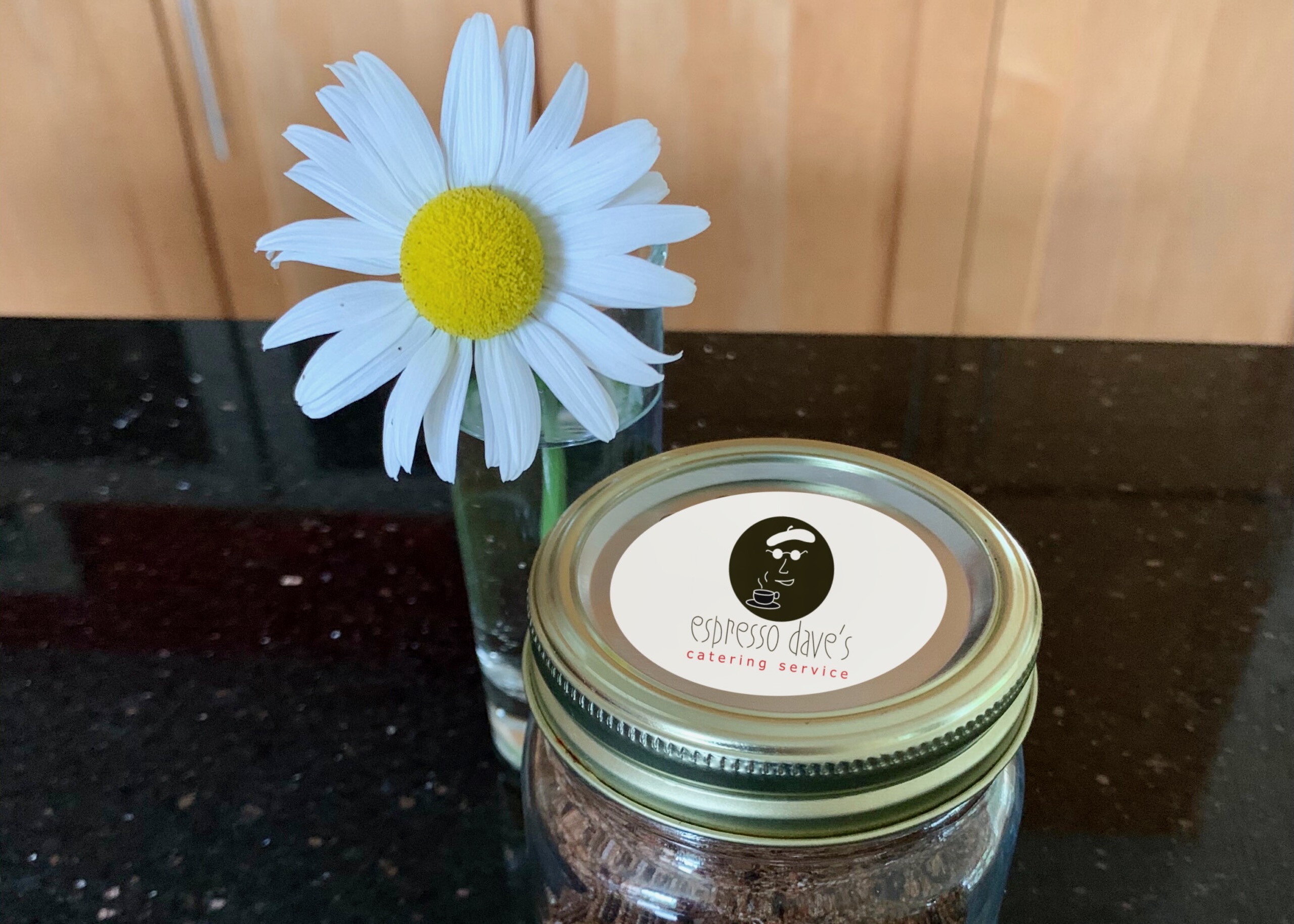 Espresso Dave’s coffee spice dry rub recipe for grilling in a sealed jar with branded label and daisy in vase on black countertop