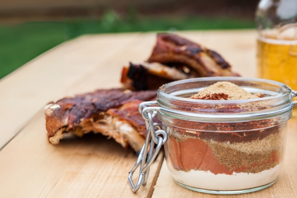 Glass jar of coffee spice dry rub with grilled ribs in background – Espresso Dave’s recipe for grilling greatness