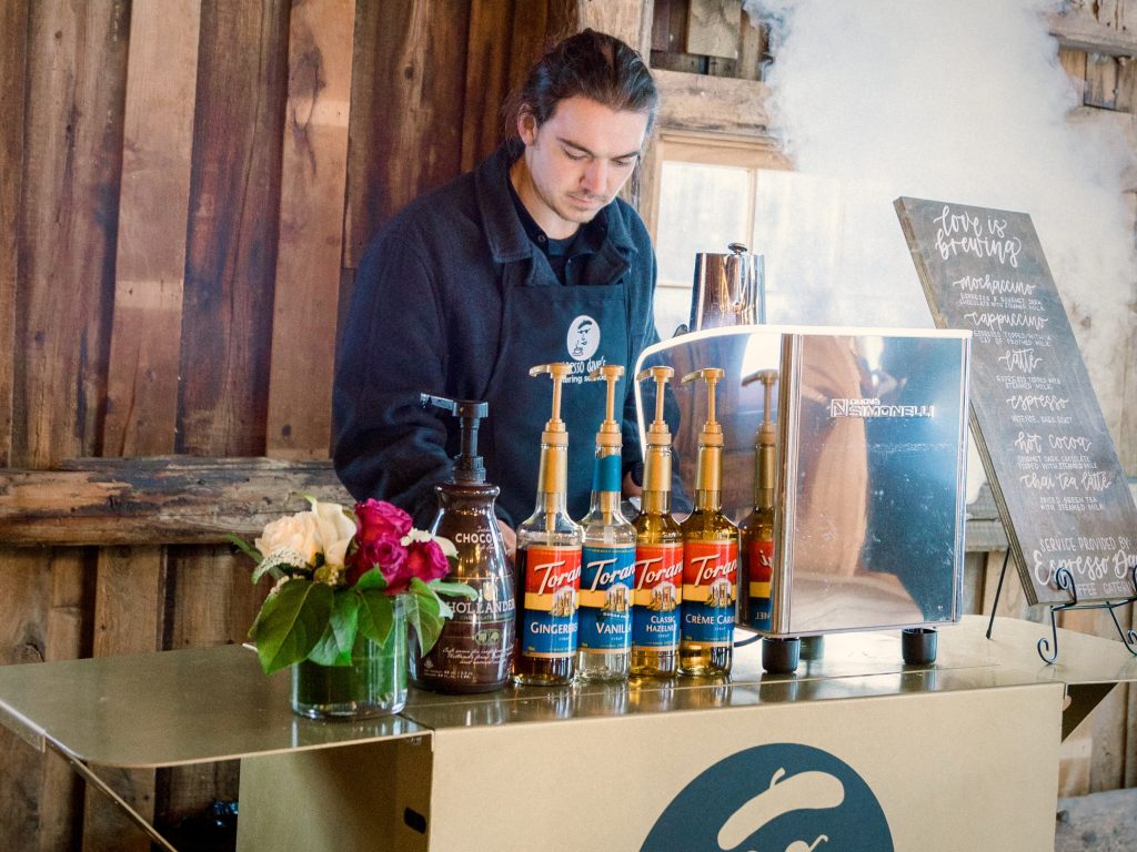 Barista preparing espresso at a rustic barn coffee bar with steam rising, showing winter wedding ideas that bring warmth and atmosphere to the celebration.